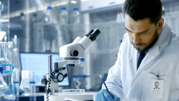 研究科学家用手术钳调整培养皿中的样本并在显微镜下观察他在一家现代化实验室工作
