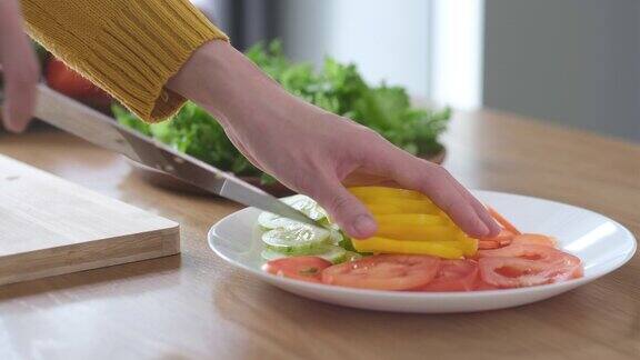 特写的妇女手准备切片黄辣椒胡萝卜黄瓜和西红柿在家里的厨房做沙拉