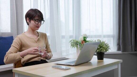 年轻女性在家边喝水边用笔记本电脑工作