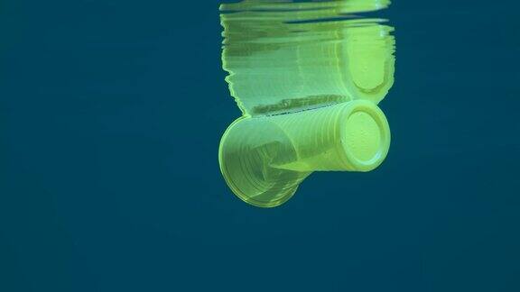 塑料污染漂浮在水下的黄色塑料杯在阳光下反射在蓝色的水面上海洋塑料垃圾环境污染问题亚得里亚海