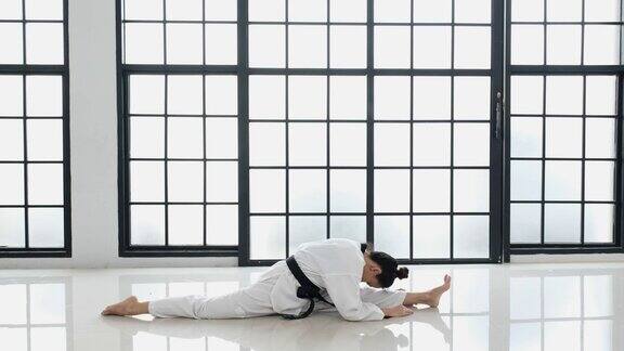一名年轻的跆拳道女孩在体操馆里表演分开双腿的动作她腰带上的文字显示的意思是跆拳道