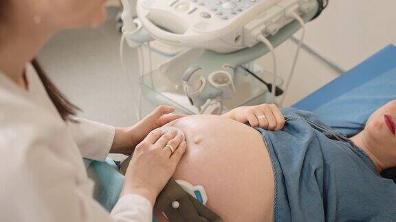俯视图漂亮的孕妇躺在医疗沙发上而称职的妇科医生检查婴儿的心跳现代化的检查设备怀孕期间的保健