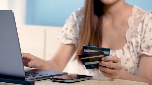 4K50fps亚洲女性手特写信用卡持卡人手里拿着三个坐在笔记本电脑前选择信用卡准备网上购物坐在床上网上购物