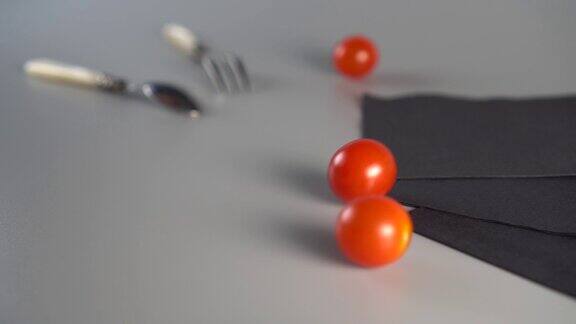 成熟的红樱桃番茄从上面落下在灰色的背景上一个勺子一个叉子和三张黑色的餐巾的静物