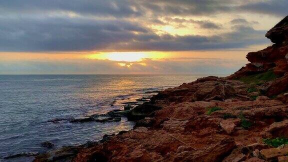 日出时的小海湾和风景如画的海滩地中海岩石海岸的红色斜坡波浪拍打着岩石海岸