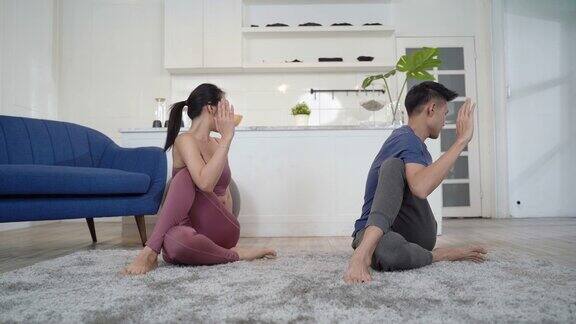一对亚洲夫妇在家里的客厅里练习瑜伽姿势