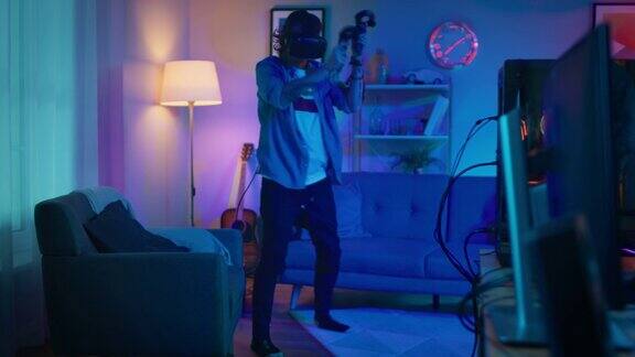 一个年轻人正戴着耳机积极地玩虚拟现实视频游戏他正站在一个温暖的霓虹灯下的舒适的房间里他挥舞双手射击和躲避障碍