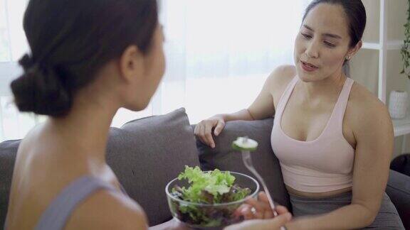 穿着运动服的健康女性正带着一种幸福的感觉吃着沙拉一名健康的亚洲女性正在饮食和卡路里拿着一碗沙拉吃健康的食物概念