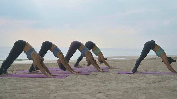 一群中年亚洲妇女穿着运动服在夏天的海滩上练习瑜伽