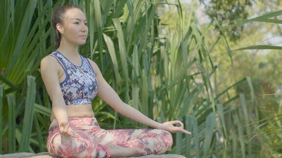一个年轻的亚洲女人在公园里做瑜伽迷人的女人在美丽的阳光下冥想莲花姿势