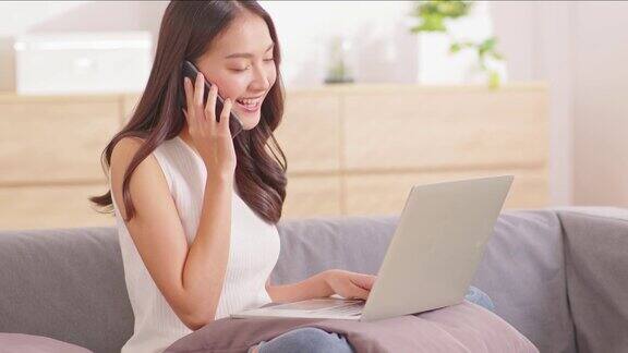 美丽的亚洲妇女穿着休闲毛衣工作在笔记本电脑上微笑并与客户在智能手机交谈以获得成功的工作在家里的想法要求自由职业妇女工作在线销售营销