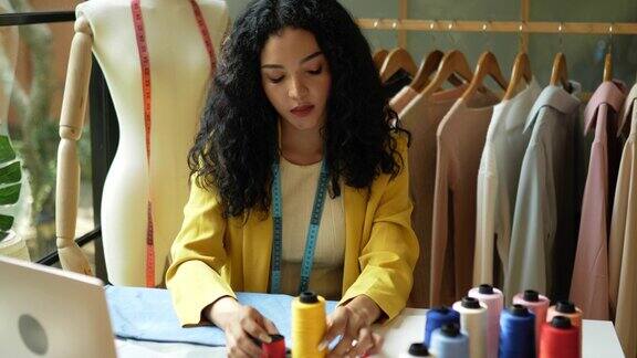 手持拍摄亚洲年轻女设计师拿着两种颜色的线决定用于缝纫的线的颜色创业小企业家