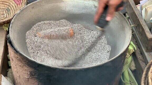 一个卖玉米的人正在用热盐烤玉米用传统的方法烤腌玉米玉米正在盐里烤