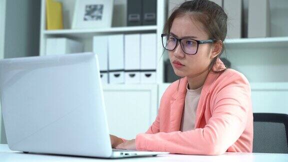 严肃的年轻亚洲女商人在办公室的桌子上使用电脑双手放在额头上