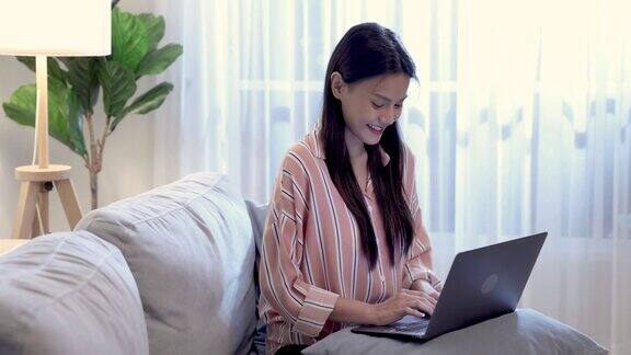漂亮年轻的亚洲女人使用电脑笔记本电脑坐在家里客厅的沙发上