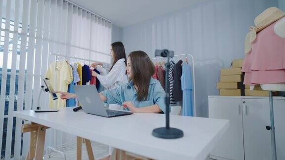 两个自信的年轻女企业主坐在她的办公室里通过笔记本电脑上的直播向她的在线客户展示新的时尚商品
