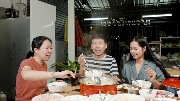 4k3个亚洲朋友在他们面前的一家餐厅吃着sukiyaki里面有sukiyaki调料和红色的sukiyaki锅