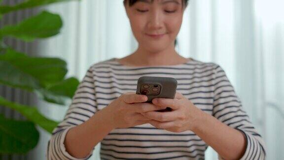 亚洲妇女开心地微笑着在家里办公室使用智能手机