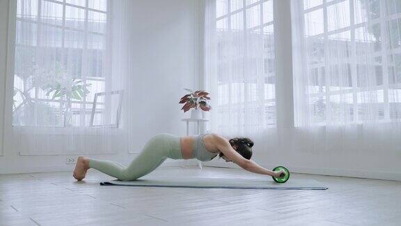 亚洲运动女人是使用滚轮式腹肌轮运动机以建立腹部和背部肌肉健身概念和健康
