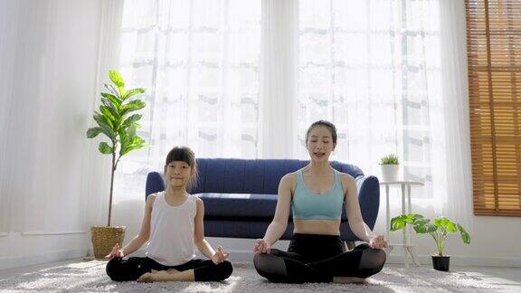 画像年轻的亚洲母亲女儿准备伸展后在瑜伽冥想妈妈和小女儿在家里的瑜伽垫上练习瑜伽一起生活母亲节理念