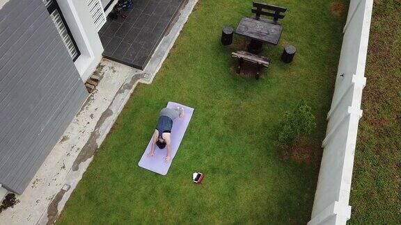 亚洲华人中年妇女练习瑜伽前院早上的房子