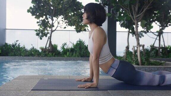 一个在泳池边锻炼的亚洲女人在垫子和体重上锻炼