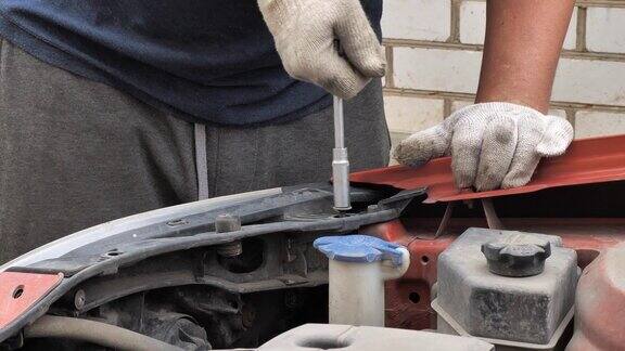 一个男人正在他家院子里的车库附近修理他的汽车一名男子用扳手拧下螺栓更换汽车上坏了的部件汽车修理厂