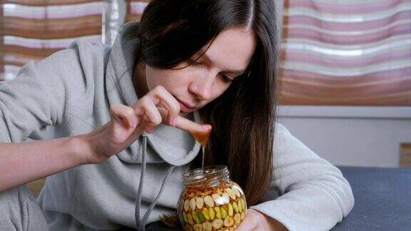 女人用手指蘸罐子里的蜂蜜和坚果从手指上吃蜂蜜