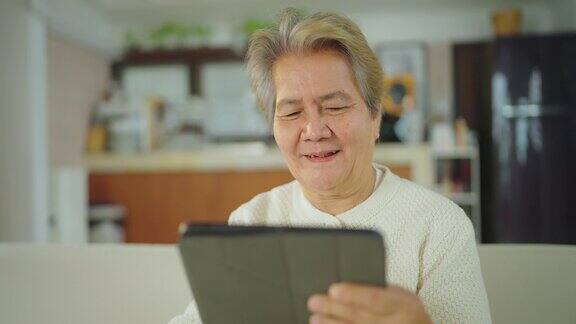 老年妇女在家里的客厅里微笑着使用平板电脑