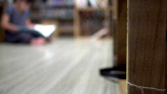 小女孩坐在木地板上看书焦点在书架上以下的脖子