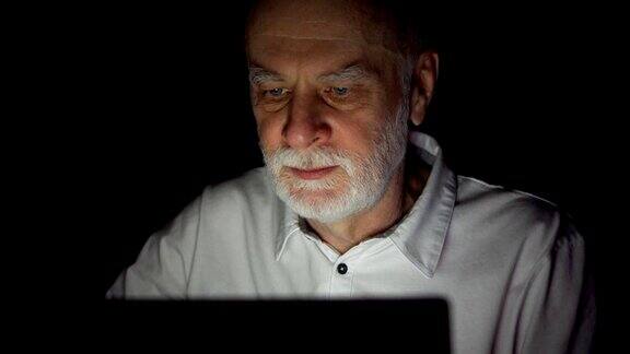 老人晚上在家里用笔记本电脑看新闻只照亮黑暗的脸