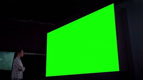 女人看着大空白绿色屏幕在黑暗的房间-色度键概念