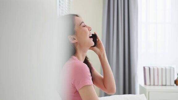 亚洲有魅力的女人早上在家的床上打电话快乐休闲美丽的女性坐在卧室里享受假期周末在家里使用智能手机与技术交流