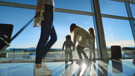 母亲和她的两个孩子望着窗外的机场大楼的玻璃墙和跑道在阳光下