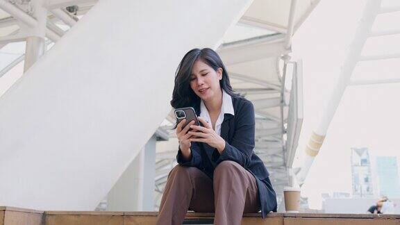 微笑的亚洲商务女性坐在商务区用手机聊天和社交媒体商务人士与同事聊天商务官员的生活方式