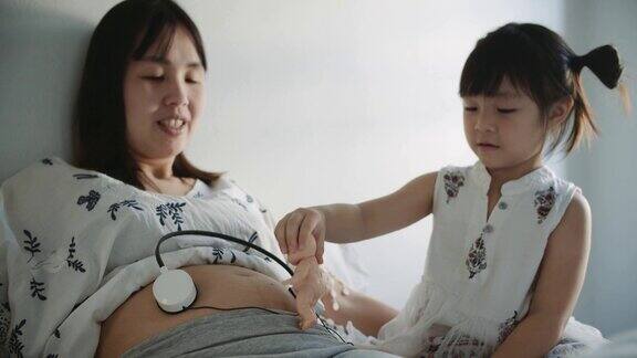 快乐的孕妇和她肚子上戴着耳机的女儿