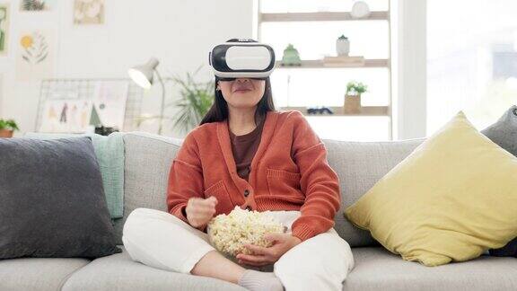 虚拟现实看电影和女人在沙发上与爆米花有趣的喜剧表演在虚拟世界赛博朋克和高科技的体验年轻人放松地坐在沙发上戴着虚拟现实眼镜边吃边笑