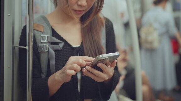 特写微笑的年轻亚洲游客在行驶的地铁列车上使用手机女性在旅行时使用手机社交媒体