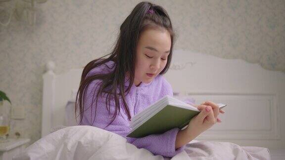 20多岁亚洲女性独自坐在床上看书穿着紫色睡衣的女性喜欢坐在床上看书