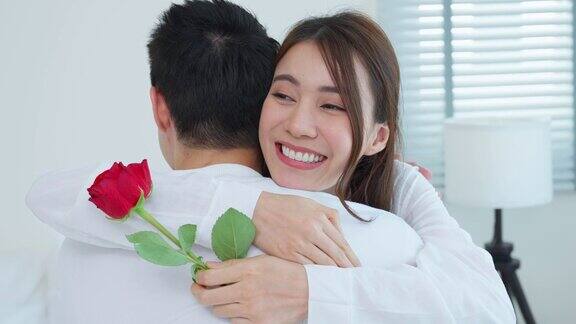 亚洲青年惊喜送玫瑰给美丽的女友迷人浪漫的新婚男女坐在床上一起享受庆祝周年纪念日和情人节