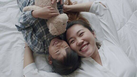 前视图家庭快乐的亚洲母亲和女儿在早上躺在床上看着相机