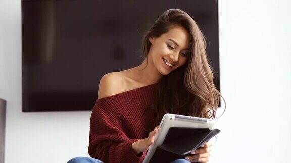 快乐的黑发女人穿着毛衣坐着用平板电脑