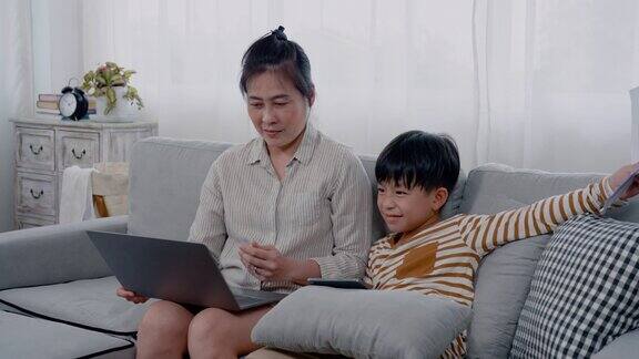 4K亚洲男孩放了一个平板电脑转身面对他的母亲打扰了正在努力工作的母亲因为他想引起她的注意母亲把纸拉开骂了儿子一顿