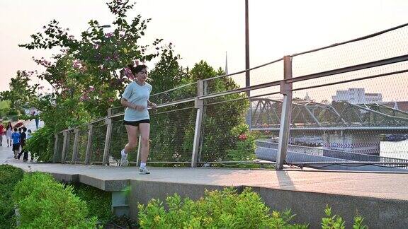 4K年轻亚洲女子在曼谷日落前在桥上跑步