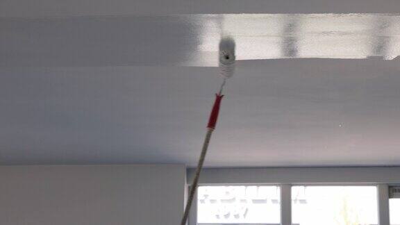 一名男子正在用油漆滚筒给自己家的天花板上油漆