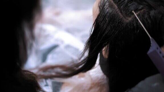 头发染色染发剂特写镜头在沙龙或发廊染发师用刷子将染发剂涂在女性深褐色发根上