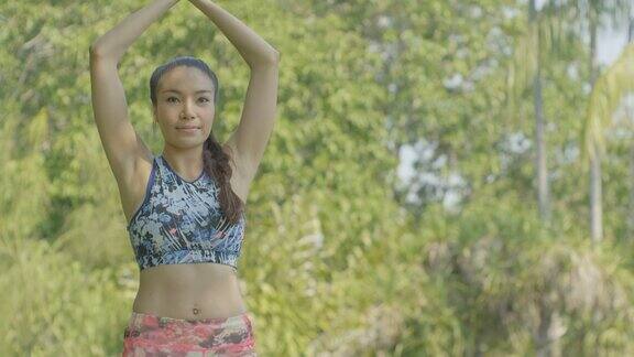 一个年轻的亚洲女人在公园里做瑜伽迷人的女人冥想站在瑜伽树姿势在美丽的阳光