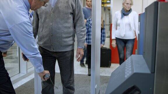 一名老人在机场通过金属探测器并被手持金属探测器扫描
