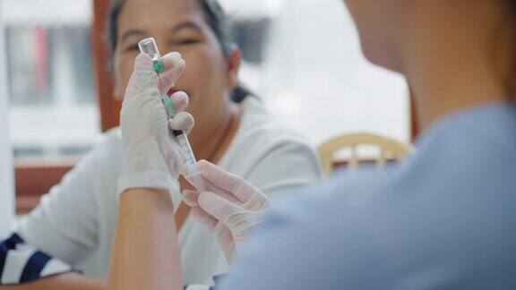 越过护士的肩膀医务工作者在注射前用注射器和手术手套准备剂量的疫苗年长的亚洲妇女害怕针头在家接受疫苗