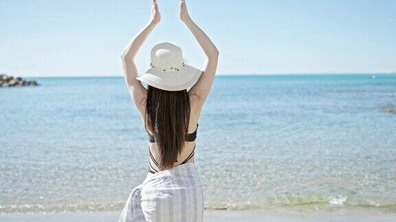 年轻的中国女游客穿着泳装和夏帽在海边做瑜伽